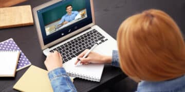 Estudante assistindo aula online e fazendo anotações em notebook.