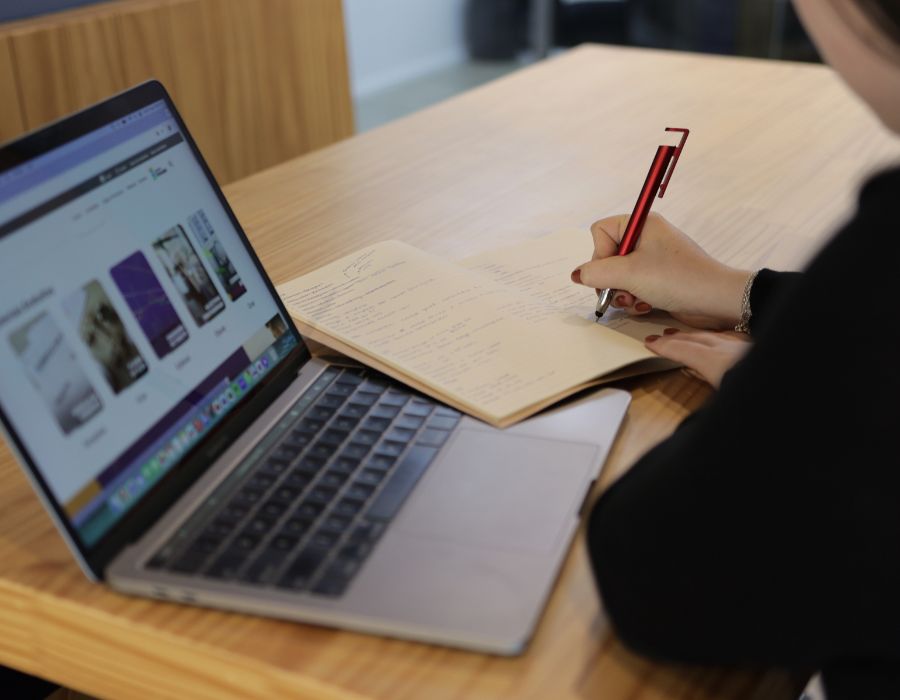 Pessoa estudando com um notebook aberto e escrevendo em caderno, analisando curso online.