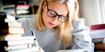 Estudante concentrada revisando um livro, focada em aprender sobre erros de concordância verbal e nominal.