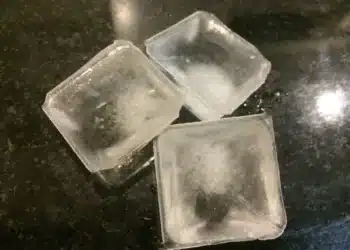 Cubos de gelo flutuando em um copo de água, com destaque para a curiosidade de como o gelo não afunda devido à sua menor densidade.