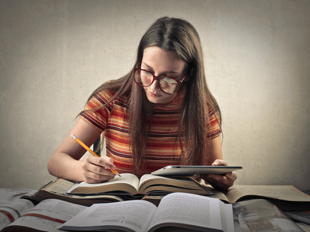 Estudante utilizando livros e tablet para estudar com apoio de plataformas digitais.