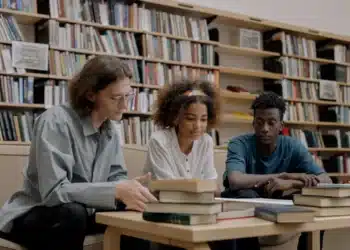 Estudantes discutindo e analisando livros e textos em uma biblioteca moderna.