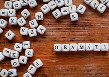 Palavra 'GRAMÁTICA' formada por blocos de letras sobre uma mesa de madeira. Saiba as regras de gramatica.