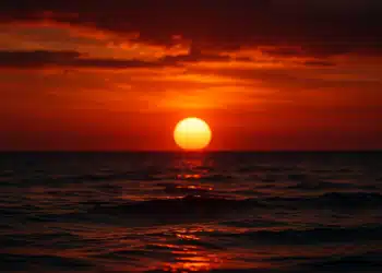 Pôr do sol sobre o mar, com céu em tons de vermelho e laranja, simbolizando a dúvida na gramatica sobre o plural da expressão.
