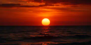 Pôr do sol sobre o mar, com céu em tons de vermelho e laranja, simbolizando a dúvida na gramatica sobre o plural da expressão.