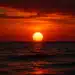 Pôr do sol sobre o mar, com céu em tons de vermelho e laranja, simbolizando a dúvida na gramatica sobre o plural da expressão.