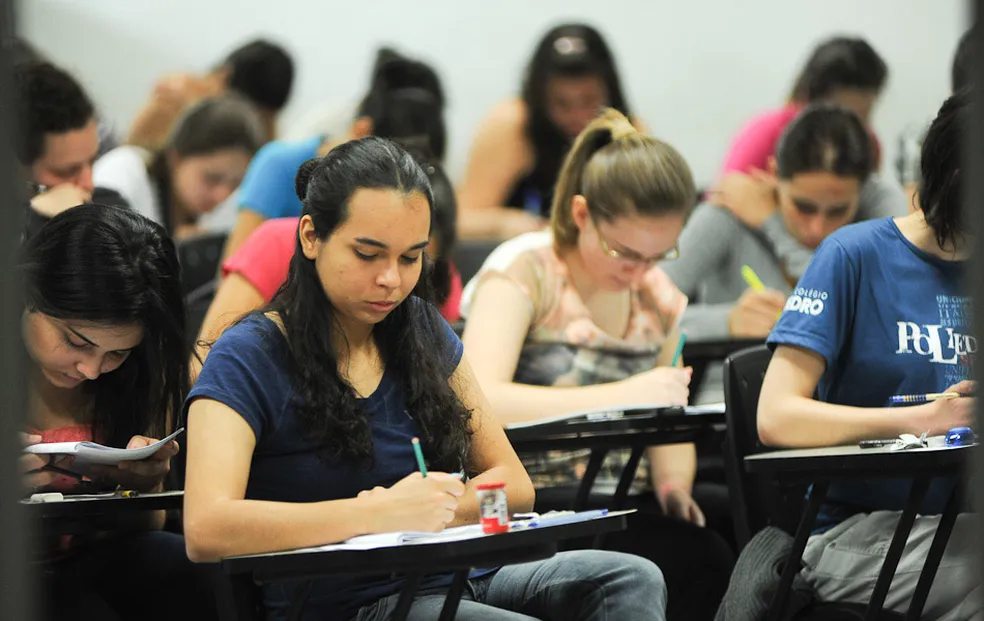 Candidatas fazendo prova em ambiente de vestibular com foco em concentração e estudo