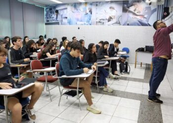 Professor ensinando em uma sala de aula cheia de alunos, simbolizando o processo de aprendizado e a preparação para o ENEM.