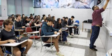 Professor ensinando em uma sala de aula cheia de alunos, simbolizando o processo de aprendizado e a preparação para o ENEM.