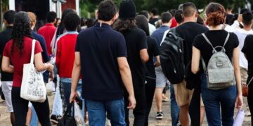 Uma multidão de jovens e adultos caminha em grupo, representando os candidatos que se preparam e comparecem às provas do ENEM.