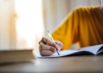 Estudante praticando redação dissertativa para vestibular 2025 escrevendo em caderno com caneta