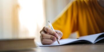 Estudante praticando redação dissertativa para vestibular 2025 escrevendo em caderno com caneta
