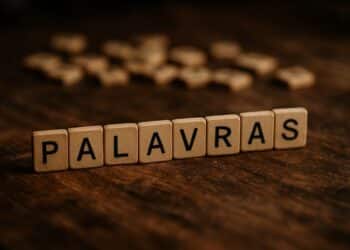 Blocos de madeira formando a palavra PALAVRAS sobre superfície de madeira escura com letras dispersas ao fundo.