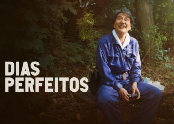O ator Kōji Yakusho no filme "Dias Perfeitos", sentado em um banco em um parque, sorrindo e olhando para cima.