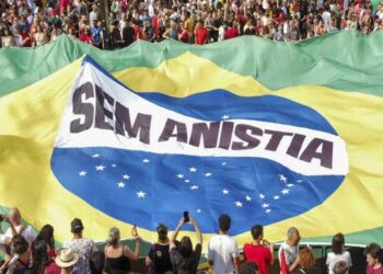 Multidão reunida em protesto com bandeira gigante do Brasil e faixa “Sem Anistia” ao centro.