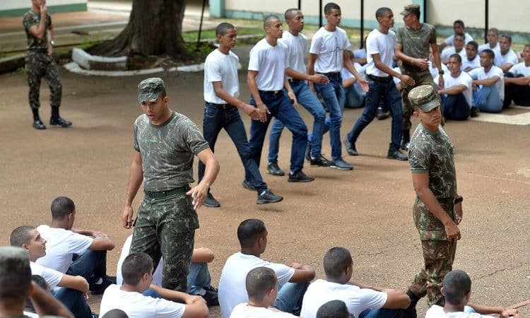 Recrutas em treinamento militar com instrutores no campo, realizando atividades de formação.