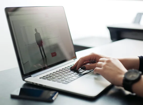  Mãos de uma pessoa digitando em um notebook, em um ambiente de trabalho ou estudo, com um celular ao lado, simbolizando o uso cotidiano do aparelho.