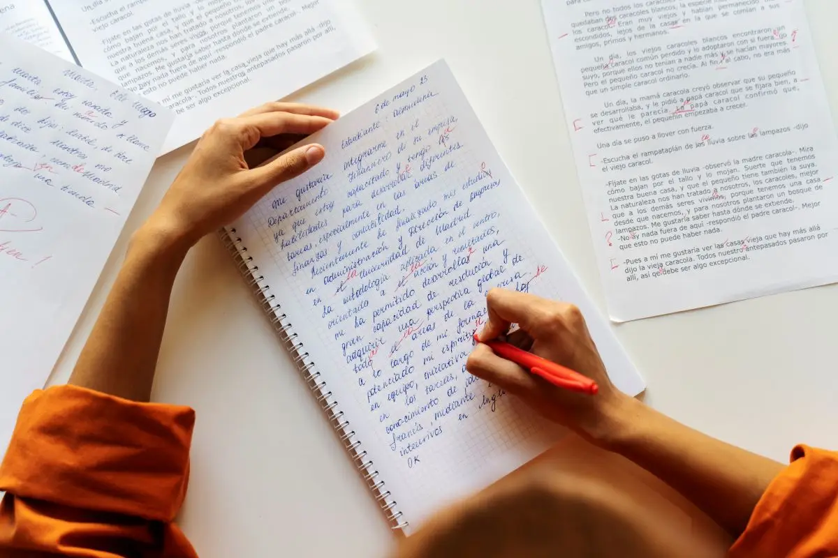 Quer se destacar no Enem? 5 truques simples para escrever sua redação de forma criativa e original 1 Pessoa escrevendo uma redação à mão, com correções em vermelho, em uma folha de caderno, ilustrando o processo de preparação para o Enem 2025.