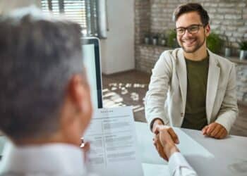 Jovem sorridente apertando a mão de um recrutador durante uma entrevista de estágio, simbolizando sucesso e profissionalismo.