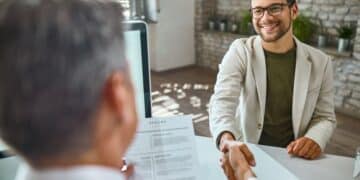 Jovem sorridente apertando a mão de um recrutador durante uma entrevista de estágio, simbolizando sucesso e profissionalismo.