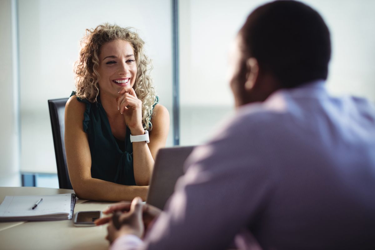 Jovem profissional loira sorrindo em uma conversa de negócios, simbolizando networking e a construção de contatos profissionais