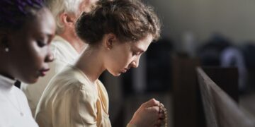 Mulher católica em oração segurando terço durante cerimônia religiosa em igreja