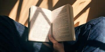 Pessoa segurando um livro aberto com páginas visíveis, em um ambiente iluminado pela luz natural.
