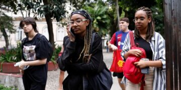 Grupo de jovens estudantes em um ambiente externo, um deles falando ao celular, ilustrando a comunicação e o acompanhamento das informações sobre o ENEM.