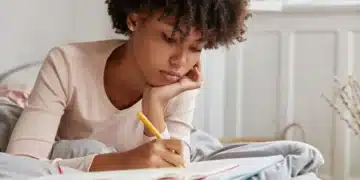 Estudante escrevendo em seu caderno, refletindo sobre dicas para redação do Enem.