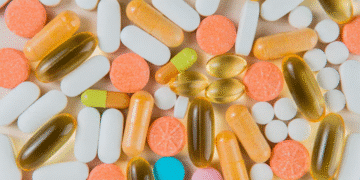 Vista superior de uma variedade de cápsulas e comprimidos coloridos, incluindo vitaminas em cápsulas amareladas e comprimidos brancos e alaranjados, simbolizando o que pode causar hipervitaminose.