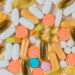Vista superior de uma variedade de cápsulas e comprimidos coloridos, incluindo vitaminas em cápsulas amareladas e comprimidos brancos e alaranjados, simbolizando o que pode causar hipervitaminose.
