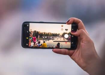 Pessoa gravando ou fotografando uma cena externa com smartphone na horizontal, evidenciando a qualidade da câmera móvel em fotos.