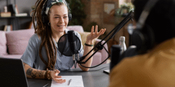 Apresentadora de podcast com microfone e fones de ouvido, gesticulando em um estúdio, ilustrando as dicas para criar e engajar uma audiência do zero.