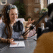 Apresentadora de podcast com microfone e fones de ouvido, gesticulando em um estúdio, ilustrando as dicas para criar e engajar uma audiência do zero.