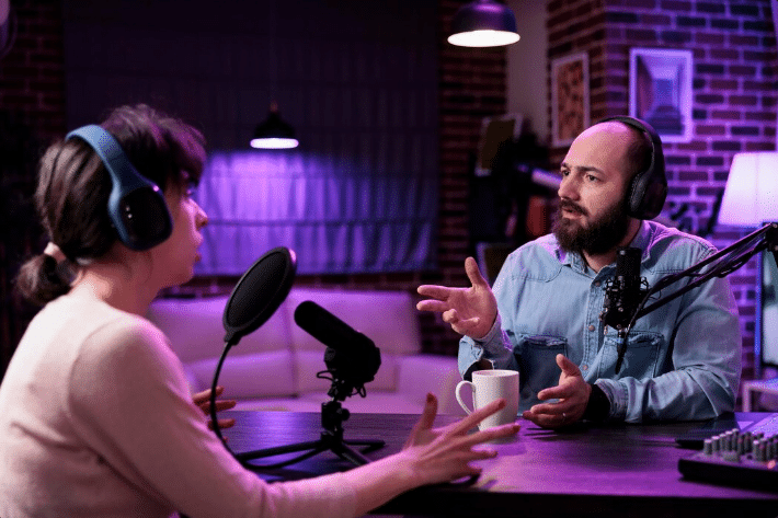 Duas pessoas (homem e mulher) gravando um podcast em um estúdio profissional, ilustrando o uso do formato por empresas para branding e comunicação com o público.