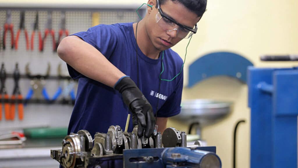 Estudante de curso técnico do Senai trabalhando em oficina de mecânica com foco em eletromecânica e equipamentos industriais.