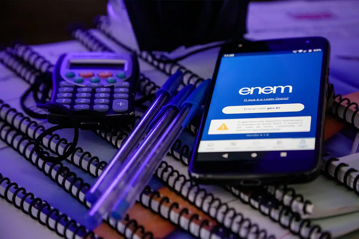 Organizando-se para o dia do Enem 2025 Smartphone exibindo a tela de login único "Entrar gov.br" para o Enem, posicionado sobre pilhas de cadernos, com duas canetas azuis e uma calculadora no plano de fundo, sob luz azulada.