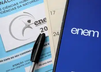 Imagem de materiais do Enem 2025, incluindo uma capa do caderno de questões, caneta e smartphone com o logotipo do Enem.