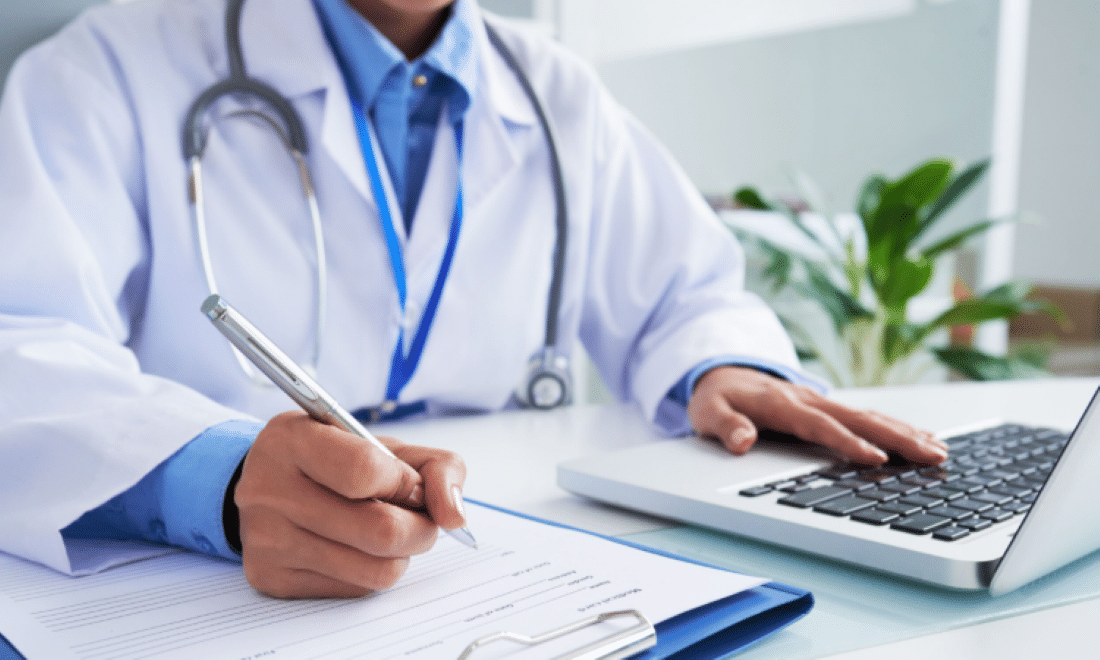 Médico preenchendo documentos e utilizando notebook.