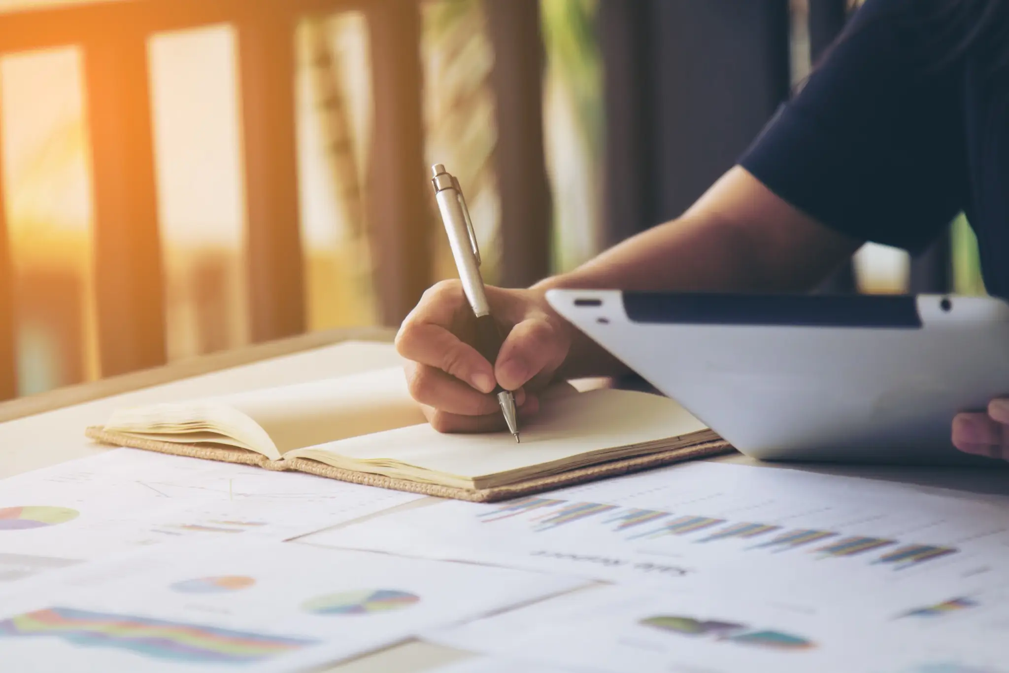 Rotina de estudos eficiente e organizada Pessoa fazendo anotações com gráficos e tablet sobre a mesa, representando planejamento e rotina de estudos organizada.
