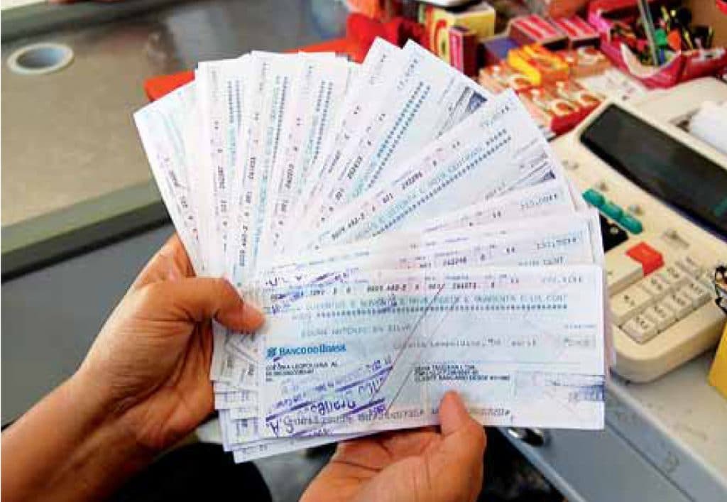 Pessoa segurando vários cheques preenchidos à mão, exemplo de prática bancária comum no passado.