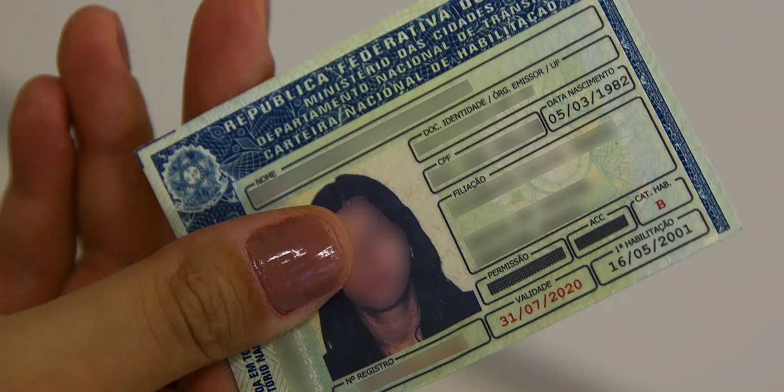 CNH Gratuita - Aulas Flexíveis Uma mão segurando a Carteira Nacional de Habilitação (CNH) física. A imagem simboliza a conquista do documento através do programa governamental de cursos gratuitos e flexíveis.