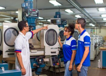 Funcionários do Senai interagindo com máquinas em um ambiente industrial, com foco em segurança e aprendizado técnico.