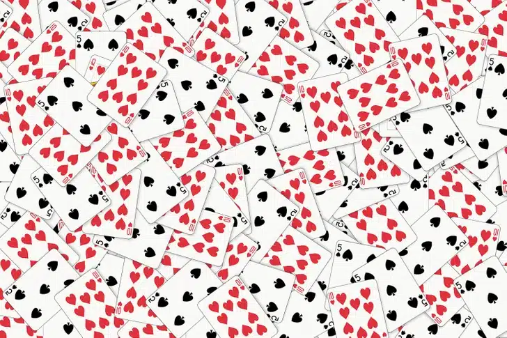 Desafio visual com muitas cartas de baralho com naipes de copas e espadas espalhadas sobre uma superfície branca.