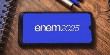 Celular exibindo a tela com o texto ENEM 2025 sobre mesa com cadernos e canetas.