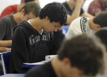 Grupo de jovens estudantes concentrados fazendo prova ou atividade em sala de aula com cadeiras azuis