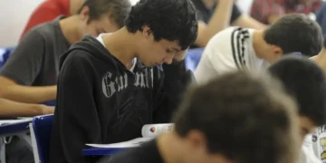 Grupo de jovens estudantes concentrados fazendo prova ou atividade em sala de aula com cadeiras azuis