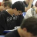 Grupo de jovens estudantes concentrados fazendo prova ou atividade em sala de aula com cadeiras azuis