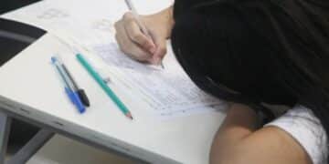 Estudante concentrada durante a prova do Enem, com a cabeça apoiada na mesa, refletindo a pressão e foco na redação.