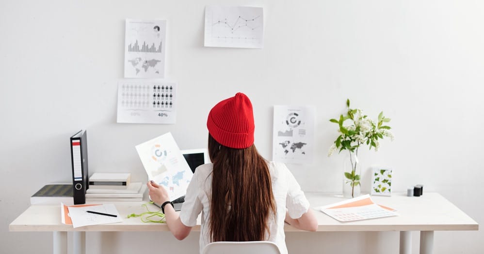Pessoa analisando gráficos e dados enquanto trabalha como freelancer, com documentos e notebook sobre a mesa.